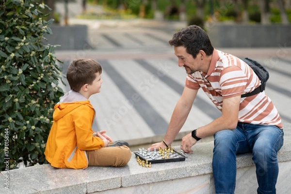 Obraz Boy with father playing chess outdoor. Learning strategic game. Education.