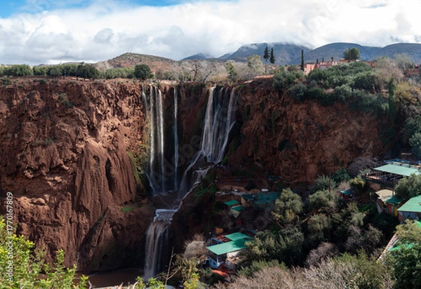 Fototapeta Ouzoud waterfalls cascade through cliffs, framed by lush greenery and blue skies.