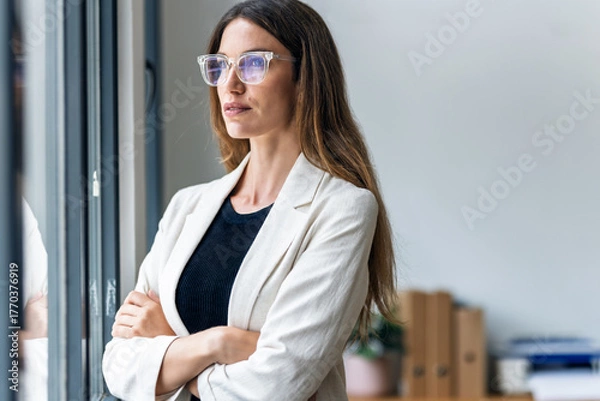 Fototapeta Beautiful businesswoman taking a break while looking forwards to the window at the office.