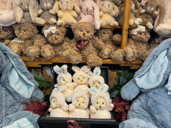 Fototapeta A charming display of various soft toy teddy bears and bunny dolls stacked on rustic wooden shelving, creating a whimsical, cozy scene.