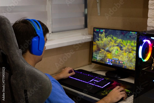 Obraz Person enjoys their free time by playing video games, wearing blue headphones for clear communication with friends while immersed in colorful, relaxing gaming environment