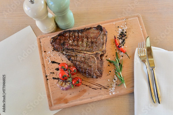 Fototapeta large steak of grilled meat on a wooden board on a table with wine
