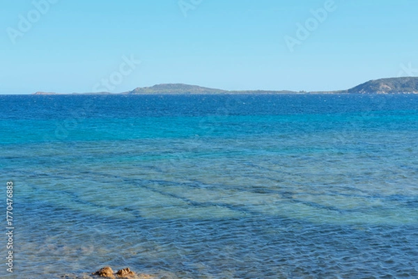 Fototapeta Wide view of a blue sea with varying shades of turquoise and islands on the horizon under a clear sky.