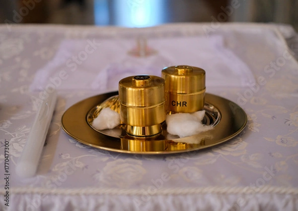 Fototapeta Golden chrism containers labeled “CHR” placed on a silver tray with cotton on an altar cloth in a church.