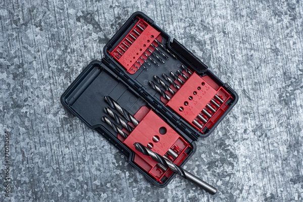 Fototapeta Drill bit set in a plastic case on a textured metal workbench. Concept for DIY, construction and repair projects.