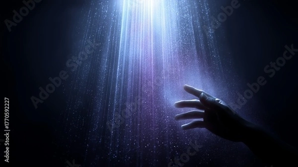 Fototapeta Reaching hand toward illuminated light rays in dark setting with moody lighting.