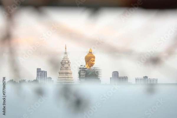 Fototapeta Big golden Seated Buddha on a blurred foreground. Statue Buddha in bangkok. A large Buddha statue in the middle of the city. There is scaffolding surrounding as construction is not yet complete.
