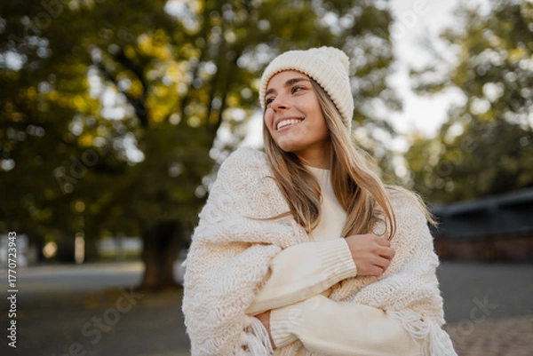Obraz attractive smiling young blond woman walking in winter park having fun in warm white knitted sweater, cape and hat, cold season