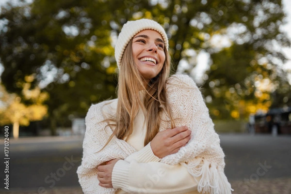 Obraz attractive smiling young blond woman walking in winter park having fun in warm white knitted sweater, cape and hat, cold season