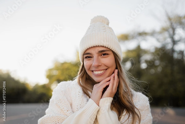 Obraz attractive smiling young blond woman walking in winter park having fun in warm white knitted sweater, cape and hat, cold season