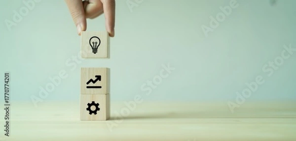 Fototapeta Concept building blocks: A hand carefully places an idea block atop a stack representing business growth and efficiency, symbolizing innovation, strategy, and progress.