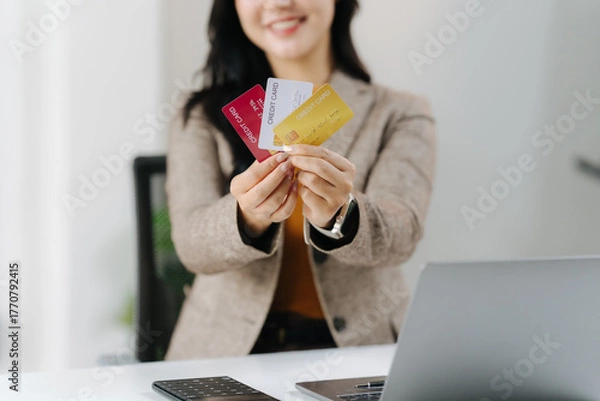 Fototapeta Payment Options: A professional businesswoman holds a selection of credit cards, showcasing diverse payment options in a modern business setting, while presenting a welcoming and friendly demeanor.