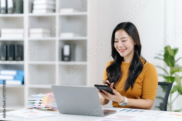 Fototapeta Focused and Flourishing: A young professional finds focus while working on a laptop. Capturing the essence of dedication and productivity in a well-lit office