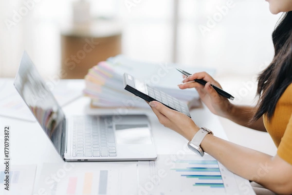 Obraz Focused Workflow: A professional concentrates on her task, meticulously reviewing documents and engaging with technology in a contemporary workplace environment.