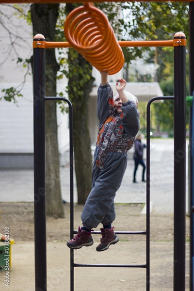 Fototapeta Little girl playing on playground, hanging walk along the monkey bars
