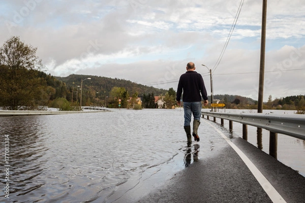 Fototapeta Man walking on the flooded road, water comes from the river Tovdalselva in Drangsholt in Kristiansand, Norway - October 3, 2017.