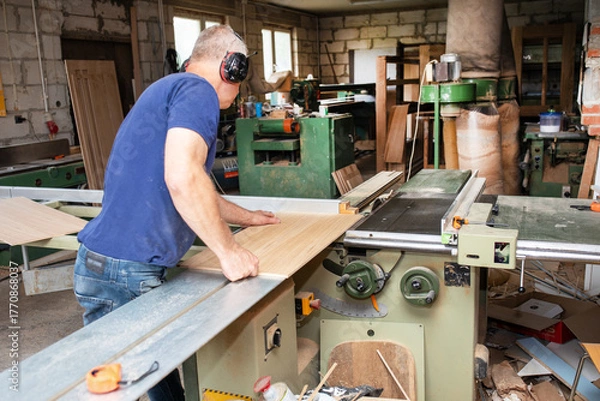 Fototapeta Carpenter working with electric saw on wooden plank in workshop. Craftsman makes own successful small business. Carpenter.