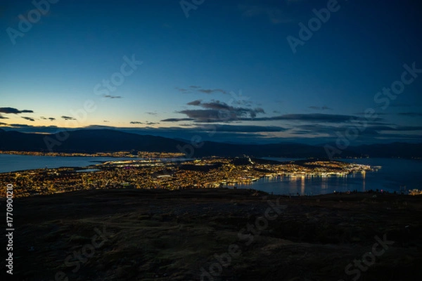 Obraz A breathtaking night view of Tromso, Norway nestled between a mountainous landscape and a calm body of water, with city lights reflecting on the water, at the top of Storsteinen