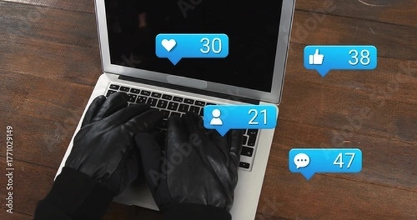 Fototapeta Typing gloved hands using silver laptop keyboard on dark wooden desk, with social media alerts