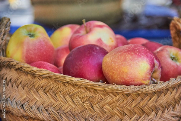 Fototapeta Fresh apples with red and yellow skin displayed in a rustic woven basket at a local Granada market in Spain, highlighting seasonal produce. autumn fruit