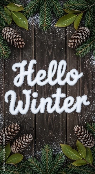 Fototapeta Festive winter composition with snow lettering spelling “Hello Winter” surrounded by pine cones, green fir branches, and scattered snowflakes on rustic dark wood, evoking cozy seasonal vibes