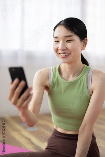 Fototapeta Smiling Woman in Activewear Using Smartphone at Home