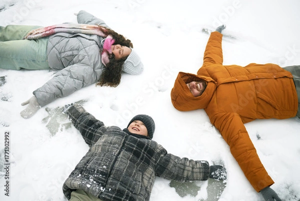 Fototapeta Caucasian man, woman and child lying on snow making snow angels, smiling and looking up, winter outdoor activity, family enjoying time together