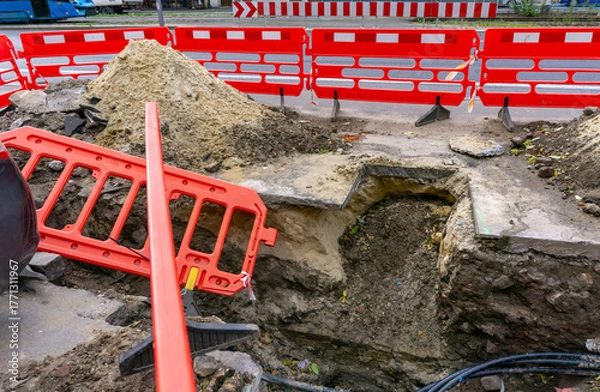 Obraz Street excavation with red safety barriers, groundworks for underground infrastructure repair, urban network modernization during road maintenance in public city area