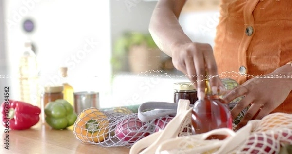 Fototapeta Torso and hands wearing orange top placing honey jar on kitchen counter, mesh bag, copy space