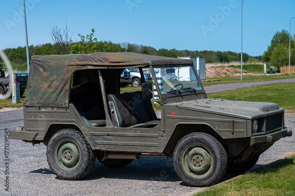 Fototapeta Military utility vehicle parked near recreational area on a sunny day