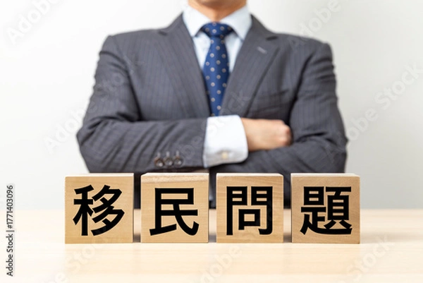 Obraz 「移民問題」と書かれたブロックと腕組みをするビジネスマン