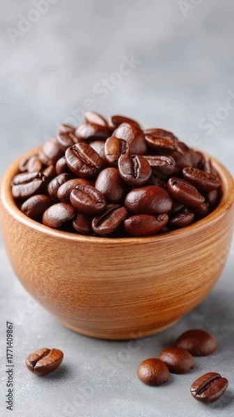 Fototapeta Close up of rich dark roasted coffee beans piled in a rustic wooden bowl with scattered beans on a textured grey surface with soft lighting and a shallow depth of field