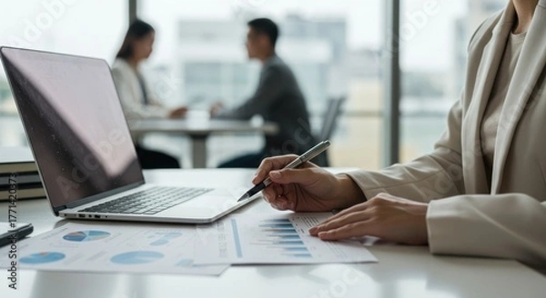 Fototapeta Woman working with laptop and documents in office setting with colleagues.