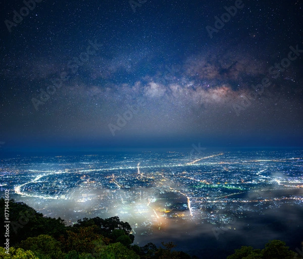 Obraz the milky way stretches across the night sky above Chiang mai city, seen from Doi Suthep mountain in northern Thailand, where city lights glow beneath layers of mist in the tranquil landscape.