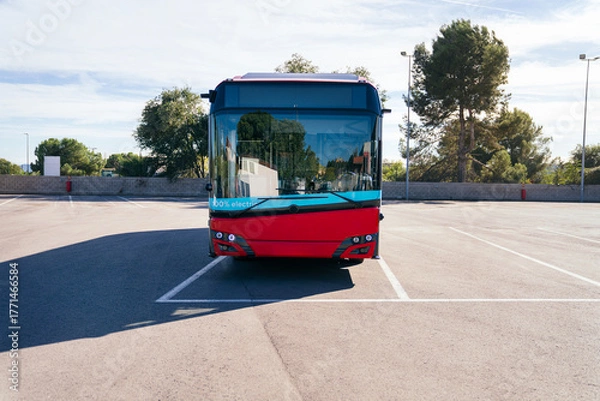Fototapeta Modern red electric bus standing in a sunny empty parking lot, representing sustainable public transport and urban mobility