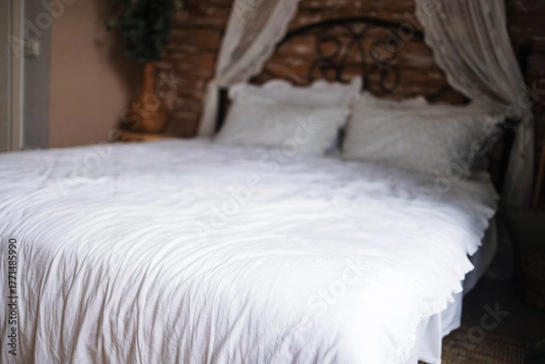 Obraz Details of bright elegant interior in cozy bedroom. Wicker side table with vase and flowers next to comfortable bed with white linen bedding. 