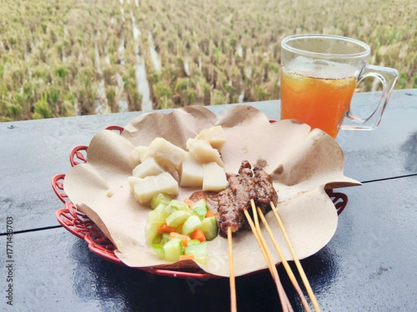 Obraz Traditional Indonesian Chicken Satay with Rice Cakes and Ice Tea in Rural Restaurant