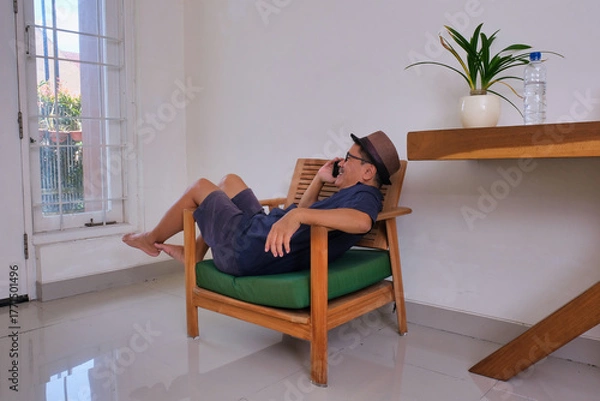 Fototapeta man casually lying on the armchair, making a phone call