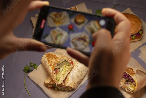 Fototapeta A person is taking photographs of a variety of food items beautifully arranged on a table with a smartphone