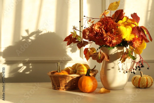 Obraz Autumn atmosphere. Vase with beautiful flowers, pumpkins and berries on wooden table near light wall, space for text