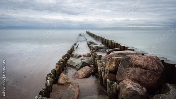 Fototapeta boulders and wooden breakwaters on the beach