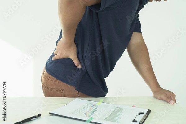 Fototapeta An asian businessman overworks and feels pain in his back from using a laptop, hand holding and rubbing hurt area, numbness in the waist area and back and a kind of health care and medical concept.	
