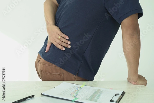 Fototapeta An asian businessman overworks and feels pain in his back from using a laptop, hand holding and rubbing hurt area, numbness in the waist area and back and a kind of health care and medical concept.	
