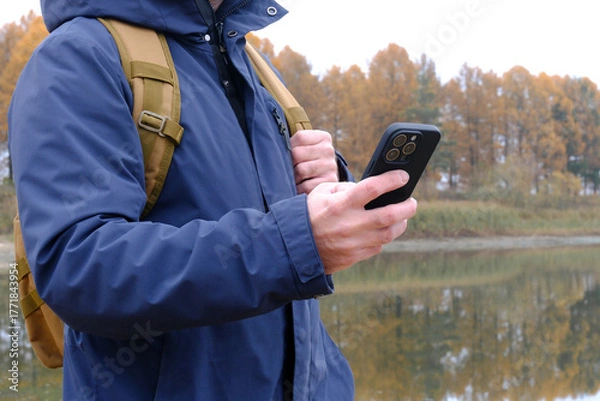 Fototapeta Hiker man using phone near autumn lake