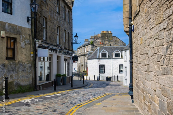 Obraz 2023-06-18 A QUIET COBBLESTONE STREET WINDING THROUGH THE QUEENSFERRY AREA OF EDINBURG SCOTLAND WITH OLD BUILDINGS AND A LIGHT BLUE SKY