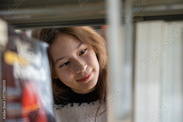 Fototapeta Close-up of young student female finding book on the bookshelf in school library