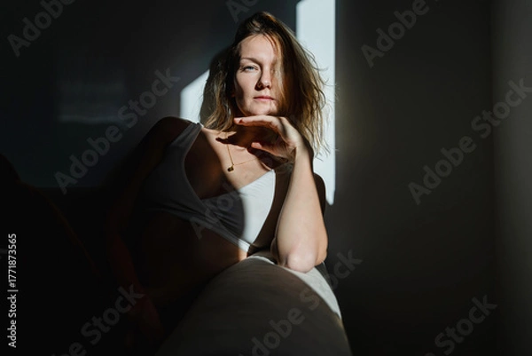 Fototapeta Deep portrait of thoughtful mature woman sitting in sunlight beam of dark room. Silhouette of sad and depressed woman at home. Concept of depression, loneliness, problems.
