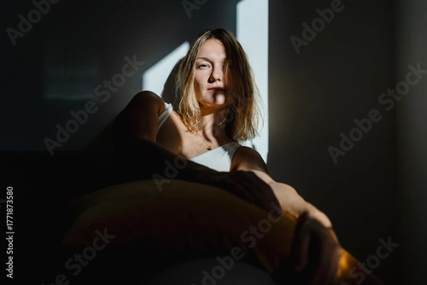 Fototapeta Deep portrait of thoughtful mature woman sitting in sunlight beam of dark room. Silhouette of sad and depressed woman at home. Concept of depression, loneliness, problems.