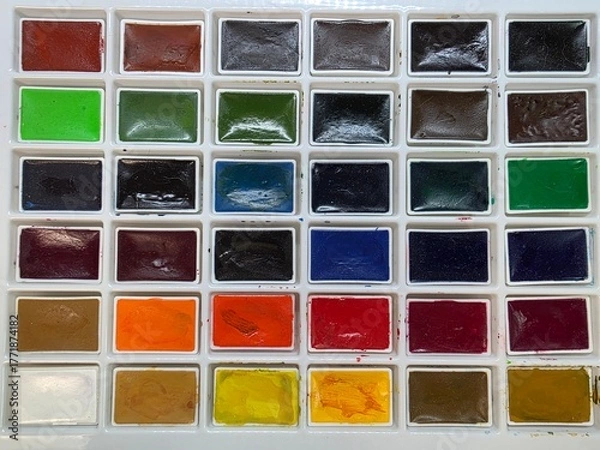 Fototapeta Full watercolor palette with assorted vibrant paint pans. Top-down view of a complete watercolor set featuring a variety of bright and dark colors in neatly arranged rectangular pans