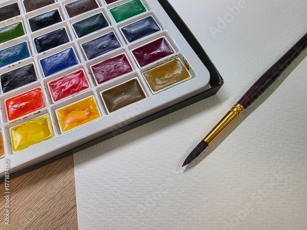 Fototapeta Watercolor paint set with brush and paper. Close-up of watercolor palette, brush, and textured paper ready for painting—perfect for art, creativity, and DIY projects